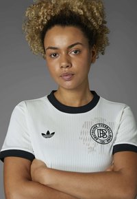 White ribbed athletic shirt with black collar and sleeve accents, featuring an Adidas logo and a circular Deutscher Fussball Bund emblem.
