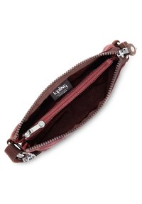 Cartera de cuero rojo con acabado texturizado, que presenta una cremallera marrón y compartimentos interiores. Incluye una etiqueta con el logo de Kipling.