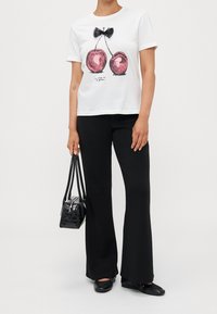 Camiseta blanca con un gráfico de cereza y un lazo negro. Combinada con pantalones acampanados negros y un pequeño bolso negro.