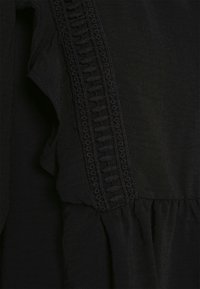 Tecido preto com uma borda franzida, delicados detalhes bordados em um padrão geométrico e textura franzida na parte inferior.