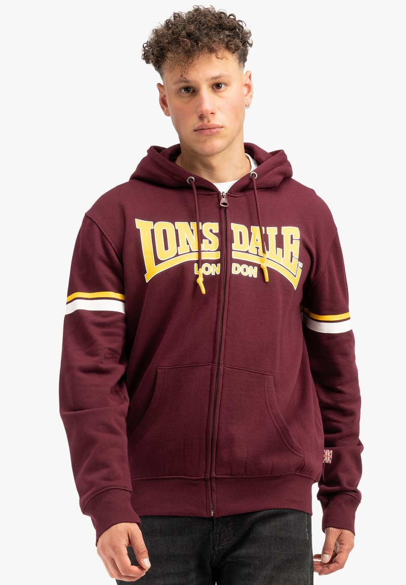 Bordový zipsový mikina s bielymi a žltými pruhmi na rukávoch, veľké logo "LONSDALE" v žltej farbe, predné vrecká a rebrovaný lem.