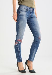 Blå denim slim fit-jeans med broderade blommor i rosa, med en klassisk femfickdesign och lätt slitna detaljer.