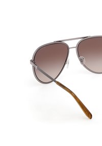 Gafas de sol estilo aviador con lentes marrones degradados, montura de metal plateado, barra de cejas texturizada y patillas de plástico marrón en forma cónica.