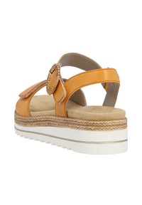 Sandale en cuir orange avec un accent en forme de fleur tissée ronde, semelle intérieure beige douce et semelle plateforme blanche texturée avec un motif en zigzag.