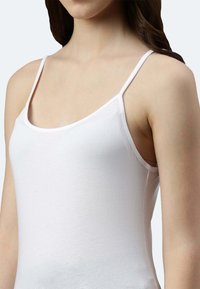 Weißes Tanktop mit dünnen Trägern, aus weichem Stoff gefertigt. Es hat ein figurbetontes Design und eine glatte Textur, die bis zur Taille reicht.