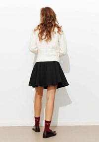 Pull en tricot blanc, jupe évasée noire, chaussettes bordeaux avec "1975" et chaussures marron ; textures lisses et couleurs contrastées.