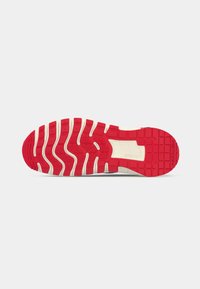 Solen på en sportssko med rød og hvid slidbane og rektangulære riller, inklusive et "Nike Free" mærke i buen.