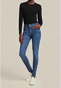 Top negro de manga larga combinado con jeans pitillo azul de talle alto y zapatillas blancas. Tela suave con silueta ajustada y diseño clásico.