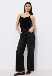 Body nero con spalline sottili abbinato a jeans neri a vita alta. I jeans presentano un design a gamba dritta e uno stile minimalista.