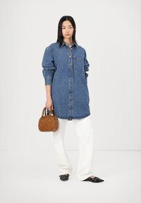 Denim srajčna obleka s gumbnim zapiranjem, žepom na prsih in dolgimi rokavi. Kombinirana z belimi širokimi hlačami in majhno rjavo teksturirano torbico.