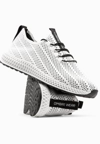 Baskets blanches en maille avec accents noirs, lacets élastiques noirs, semelle blanche texturée, portant la marque "OMBRE WEAR" sur la languette du talon.