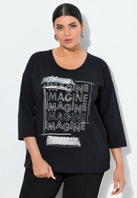 T-shirt nero a maniche lunghe con scollatura rotonda e un design grafico "IMAGINE" con accenti metallici e stampa testurizzata.