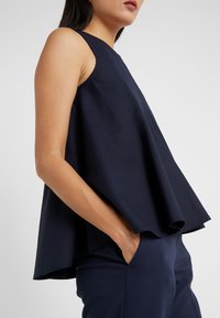 Marinblå ärmlös topp med utställd design, gjord av texturerat tyg, med rundad halsringning och avslappnad passform.