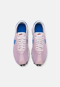 Nike sportiniai bateliai šviesiai violetinės spalvos, pagaminti iš tinklinės ir zomšinės medžiagos, su mėlynais akcentais, baltais raišteliais ir juodu guminio paviršiaus padu, užtikrinančiu sukibimą.