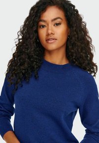 Sinine kudumiga kampsun ümmarguse kaeluse, pikkade varrukate ja tekstuurse pinnaga. Kangas näeb välja pehme ja veidi helesinise varjundiga.