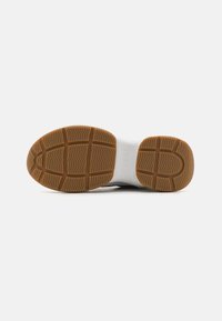 White sneaker sole with patterned rubber for traction. Features a smooth texture with embossed "GUESS" logo. Includes a brown gum rubber outsole.