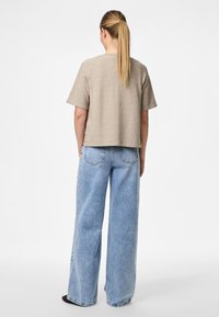 T-shirt cropped bege com mangas curtas, combinada com jeans de perna larga azul claro de cintura alta. Textura suave, design minimalista e ajuste casual.