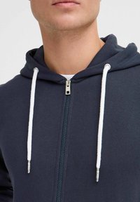 Mornarica zip-up dukserica s kapuljačom na vezanje, srebrnim zatvaračem i bijelim užetom. Mekana tkanina s glatkom teksturom.