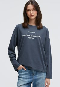 Dunkelgraues langärmliges Shirt mit Rundhalsausschnitt, auf der Vorderseite bedruckt mit weißem Text "LIEBE ÜBER ALLES . FÜR IMMER".