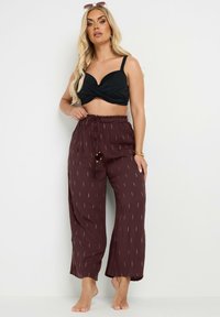Top negro de estilo envolvente con tirantes finos, combinado con pantalones sueltos burdeos que presentan una sutil textura con patrón dorado y cinturilla elástica.