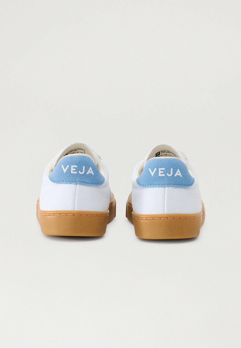Zapatillas de lona blancas con acentos en el talón de color azul claro, suelas de goma beige y el logotipo "VEJA" en la parte posterior. Diseño simple y minimalista.