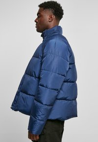 Navy blue puffer jacket with a high collar, quilted texture, and snap-button closures. Features a relaxed fit and smooth satin finish.