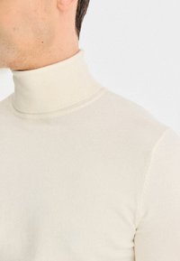 Jasno beżowy sweter z golfem wykonany z miękkiego, elastycznego materiału. Posiada dopasowany krój z prążkowanym kołnierzem i gładką fakturą.