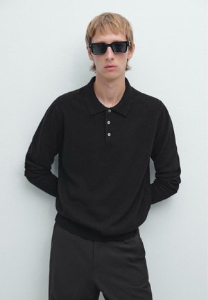Polo nero a maniche lunghe in maglia, con colletto e tre bottoni. Indossato con occhiali da sole neri. Design semplice e aderente su uno sfondo neutro.