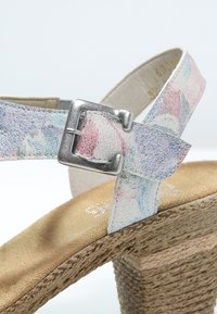 Avoin varvas espadrillesandaali, jossa on pastelinvärinen kukkakuosi, metallinen solki ja kudottu juuttityylinen korko. Pehmeä materiaali ja teksturoitu pohja.