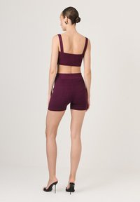 Prążkowany, dwuczęściowy zestaw w głębokim burgundzie, z krótkim topem na szerokich ramiączkach i szortami w wysokim stanie, dopełniony eleganckimi czarnymi szpilkami.