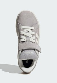 Sneaker en suède gris avec des accents blancs, lacets, sangle réglable et un design de bout arrondi. Dispose d'un intérieur rembourré et d'une semelle en caoutchouc.