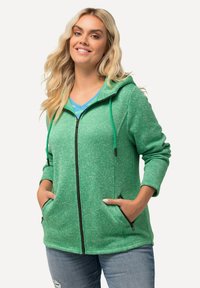 Grön zip-up hoodie gjord av texturerad tyg, med två dragkedjefickor, en dra-i-snodd huva och ett kontrasterande innerlager.