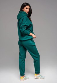 Sudadera verde y pantalones jogger a juego confeccionados en tejido suave. Presenta capucha, puños elásticos y bolsillos laterales. Zapatillas con acentos en tonos pastel.