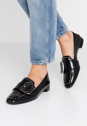 Sorte læder loafers med rund tå, dekorativ spænde, nistret detaljer langs tåhetten og en lav hæl. Stylet med opsmøgede blå jeans.