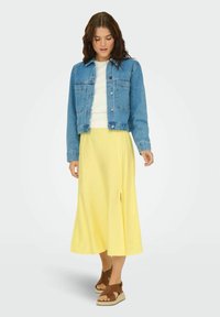 Chaqueta de mezclilla, blusa blanca y falda midi amarilla con una abertura lateral. Sandalias de esparto verdes completan el conjunto.