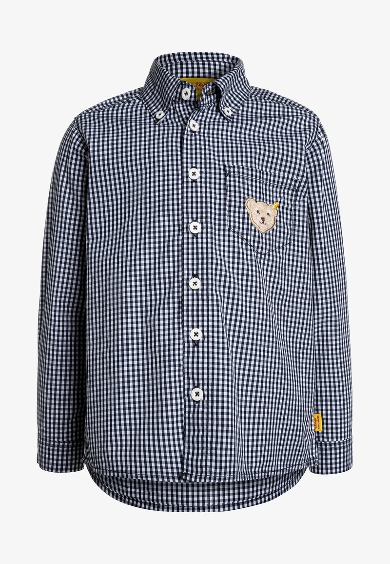 Chemise à manches longues à carreaux noir et blanc avec boutons, avec un petit écusson d'ours en peluche sur la poche poitrine et une étiquette jaune près de l'ourlet.