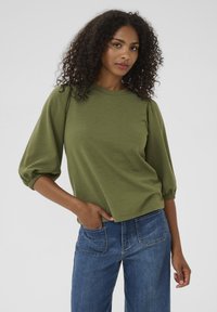 Grøn tekstureret top med rund hals og puffærmer, parret med blå denimjeans. Den tætsiddende design fremhæver en afslappet silhuet.