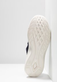 Baskets légères avec une tige en mesh bleu marine respirant, dotées d'une semelle extérieure en caoutchouc crème avec un motif texturé antidérapant et un détail de marque.