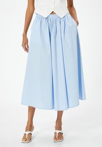 Falda de algodón azul claro con cinturilla elástica, que cuenta con bolsillos laterales y un diseño completo y fluido. Se lleva con sandalias blancas.
