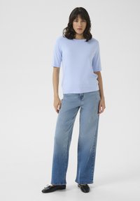 Un haut léger bleu clair à manches courtes associé à un jean bleu clair à jambes larges et des chaussures noires. Le haut présente un col rond et une texture douce.