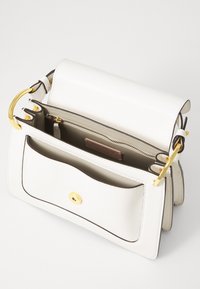 Witte leer handtas met gouden hardware, gestructureerd ontwerp, voorvak met drukknoopsluiting en een binnenvak met rits.