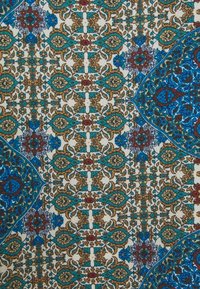 Motivo floreale e geometrico intricato su un tessuto con colori teal, blu, beige, marrone e rosso che formano disegni simmetrici e ripetuti.