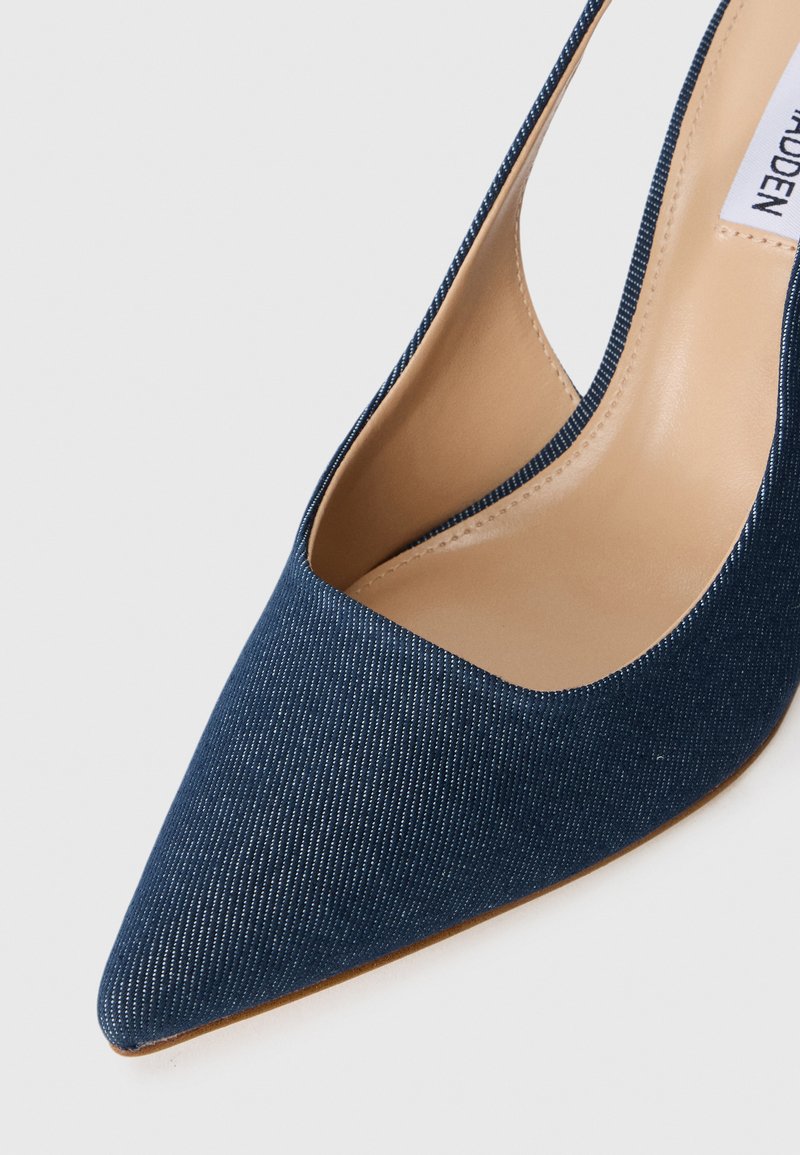 Chaussure à talon haut en denim avec un bout pointu et des côtés ouverts. Tissu bleu foncé présentant une texture légèrement côtelée. Accent de semelle intérieure beige.