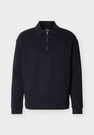 Črna polo majica z dolgimi rokavi iz mehke tkanine, z zadrgo na vratu, žepom na prsih in klasičnim ovratnikom.