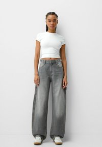 Grå vida jeans med en urtvättad finish, med sidofickor och hög midja, parat med en figurnära vit kortärmad topp och vita sneakers.