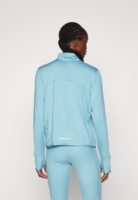 Lichtblauwe sportjack met een hoge kraag, lange mouwen, naadloos schouderontwerp en reflecterende details aan de zoom.