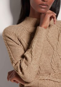 Beige gebreide trui met kabelpatroon, geribbelde kraag en manchetten, zachte textuur, met een relaxed fit en mouwen van gemiddelde lengte.