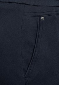 Navy blue-fabrikk joggere med en jevn tekstur, med en frontlomme med en synlig sølv knapp og sømdetaljer på siden.