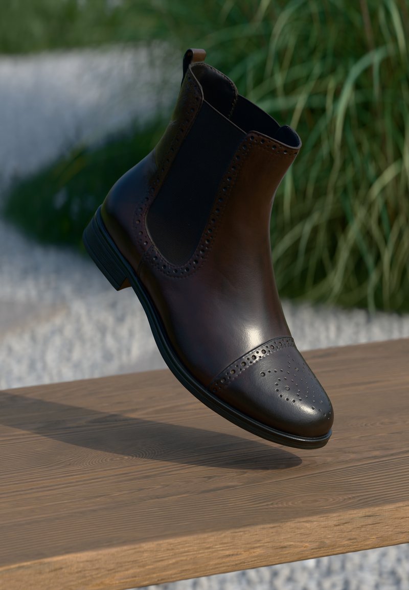 Botină din piele maro, cu laterale elastice, detalii decorative de brogue pe vârf și un tocul jos pe un suport din lemn.