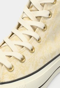 Ψηλή αθλητική μπότα από υφασμάτινο λευκό καμβά με υφή, χρυσές θηλιές, κρέμα κορδόνια και χαμηλό μαύρο καουτσούκ σόλα.